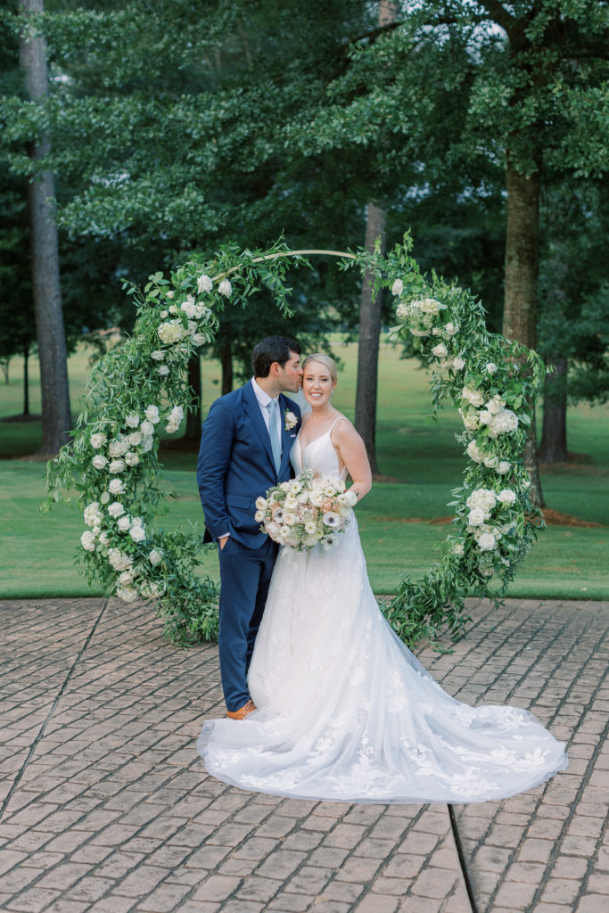 bride and groom with circular wedding arch of greenery and white flowers