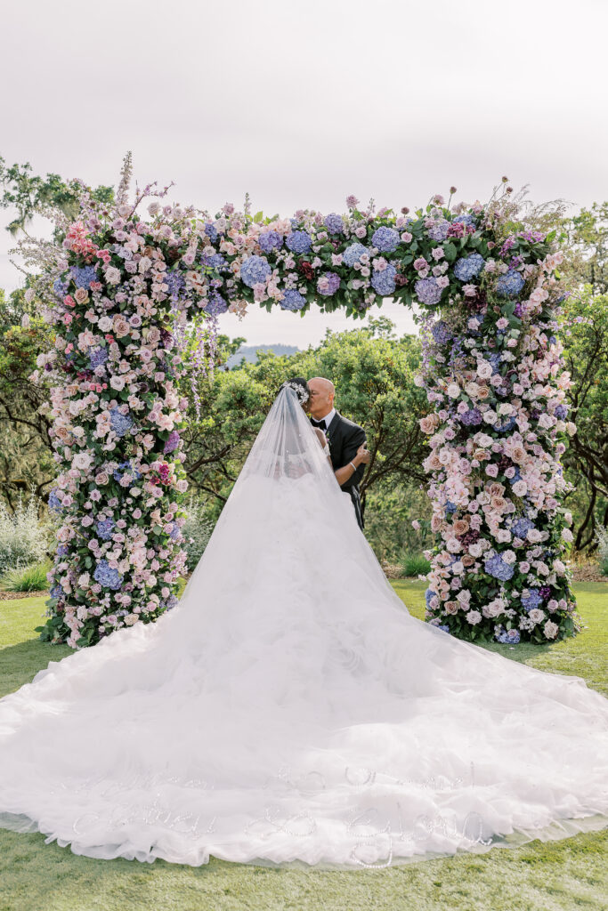 bride and groom kissing under a floral arch