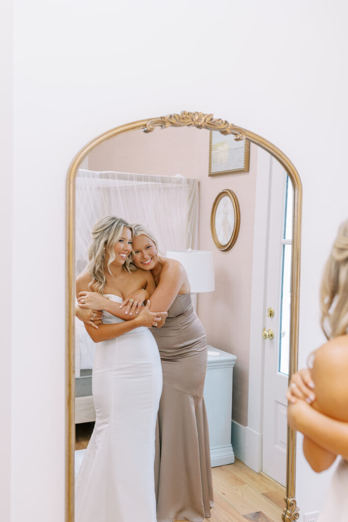 bride being hugged by her bridesmaid in a mirror