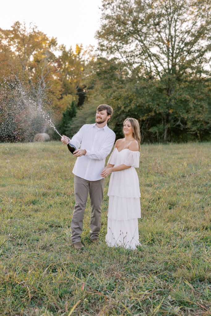 a couple having an engagement photography session in a field during golden hour with champagne