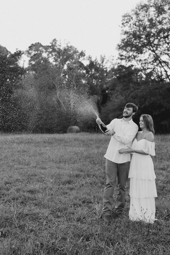 a couple having an engagement photography session in a field during golden hour with champagne