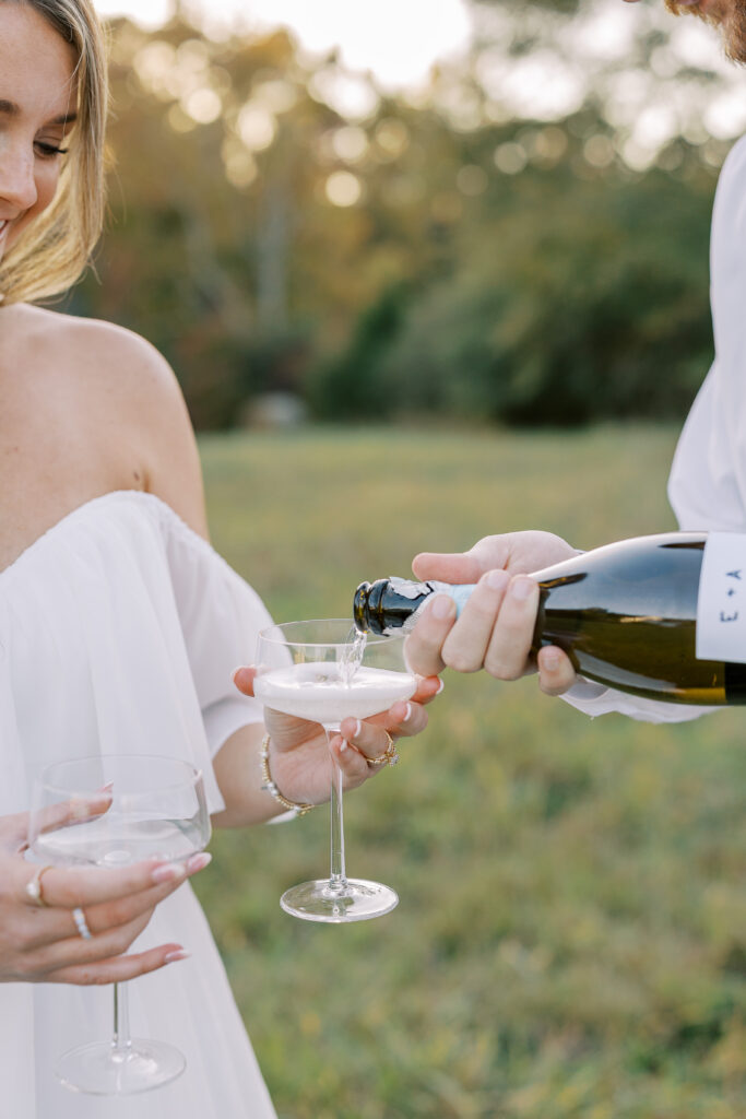 a couple having an engagement photography session in a field during golden hour with champagne