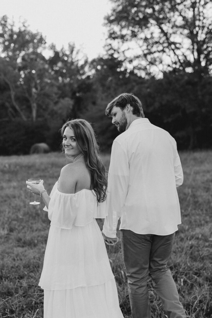 a couple having an engagement photography session in a field during golden hour with champagne