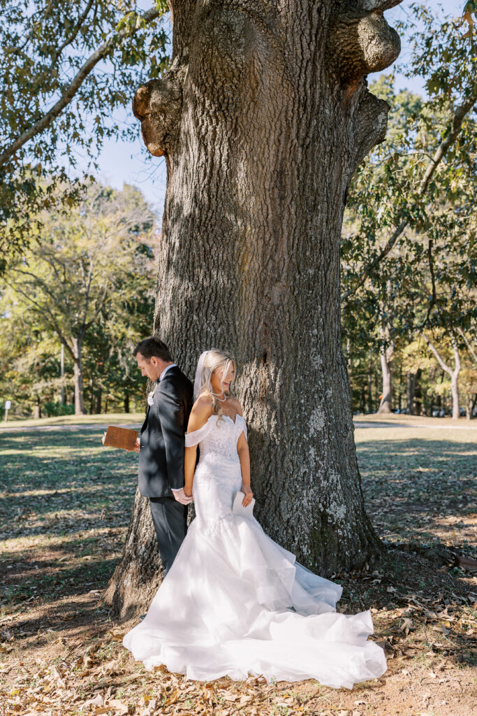 a bride and groom reading vows to each other by a tree