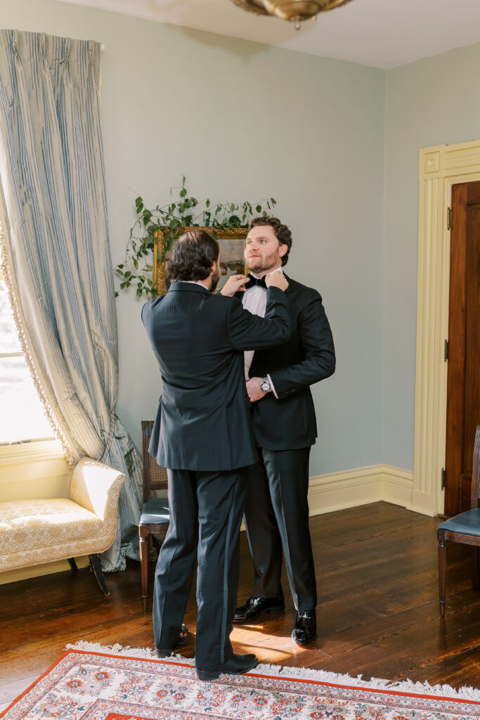 groomsman helping groom with bowtie