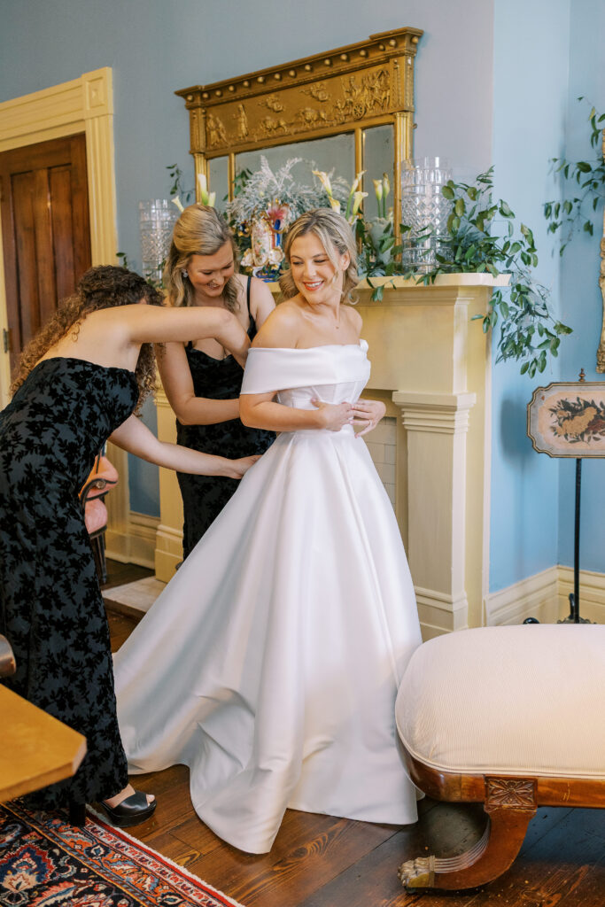 bridesmaids helping bride put on wedding dress