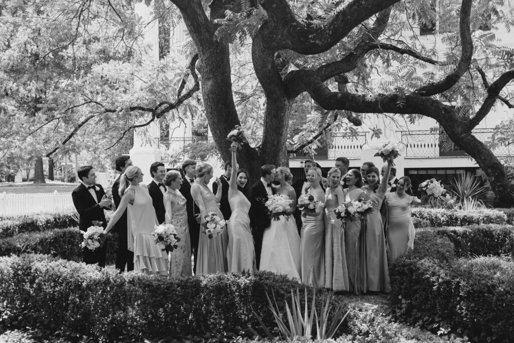 wedding party celebrate around a kissing bride and groom